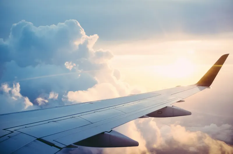 Airplane wing flying above clouds at sunset representing travel rewards