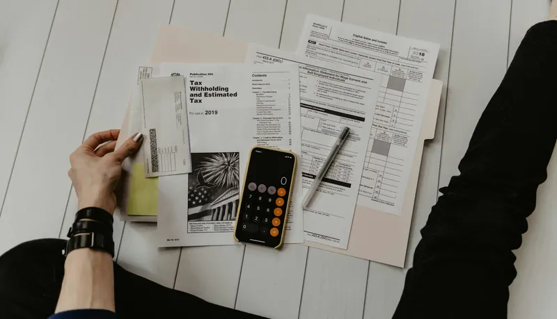 Person writing in a budget notebook with calculator and pen on a desk